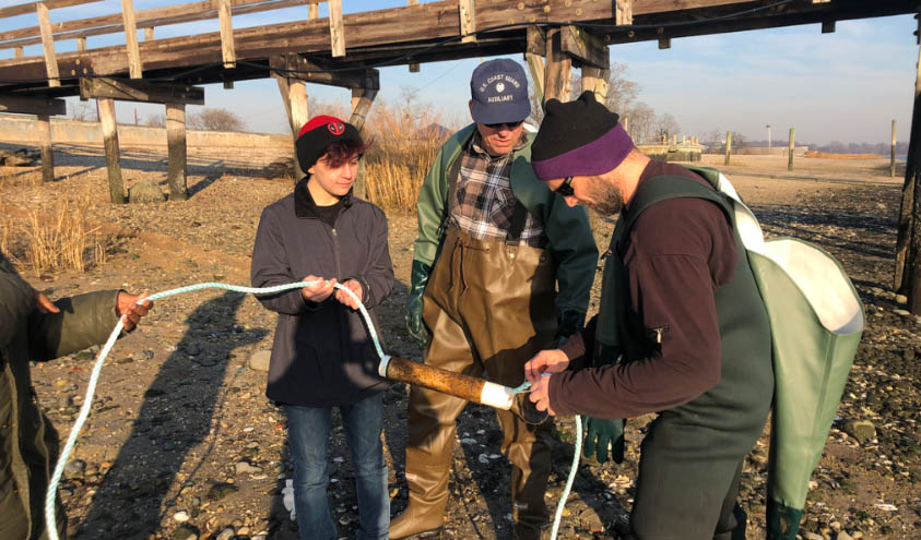 The photo shows Professor Aaron Freeman holding a long line as he prepared to seed it with juvenile kelp seed. His research team looks on. The image was taken on land near the Oyster Bay site where the line will be dropped into the water.