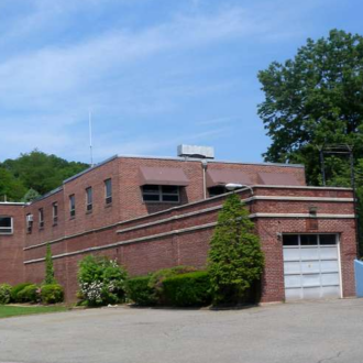 A brick building surrounded by green trees on pavement.
