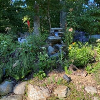 A backyard garden with a stone waterfall in the shade.