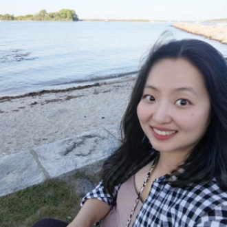 A young asian woman poses for a selfie with the beach in the background.