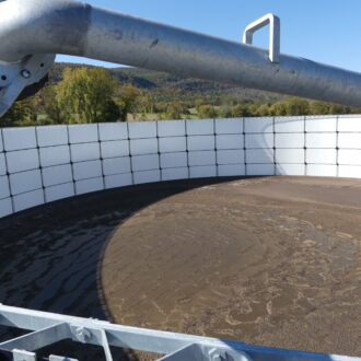 Brown manure sludge in a large round structure with a silver pipe.