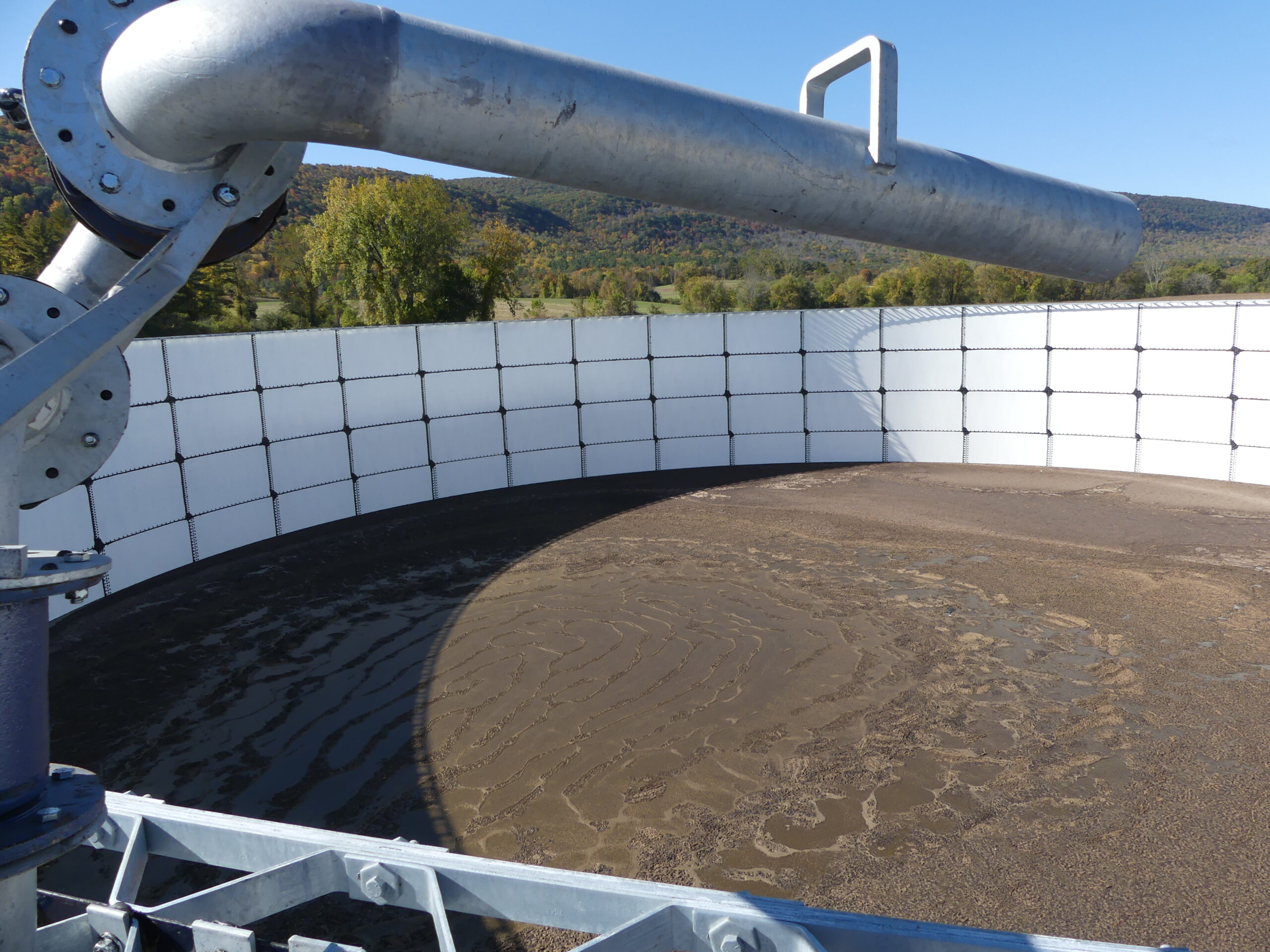 Brown manure sludge in a large round structure with a silver pipe.
